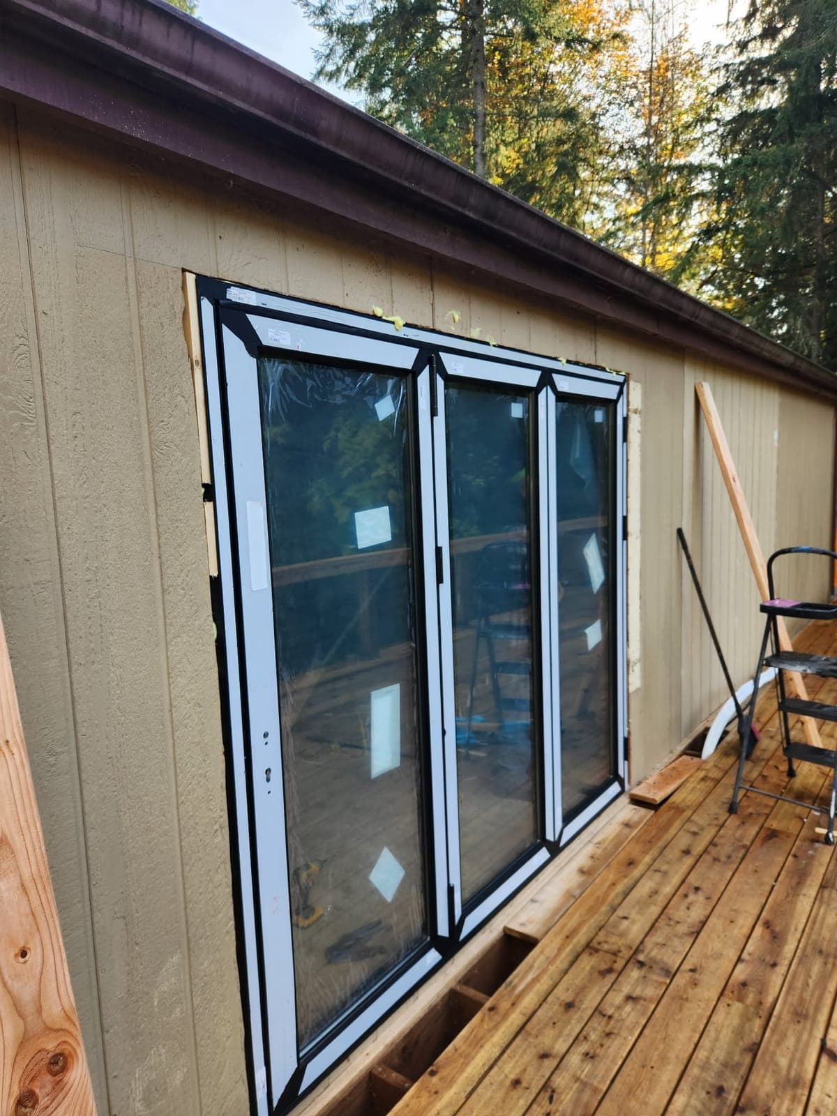 Black-framed folding glass door unit in a tan exterior wall, opening onto a wood deck