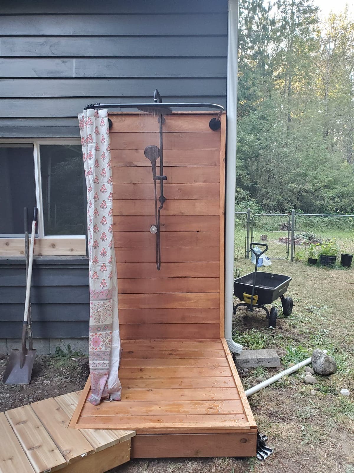 Custom cedar outdoor shower with a black rain shower head, built against dark board siding on a cedar platform