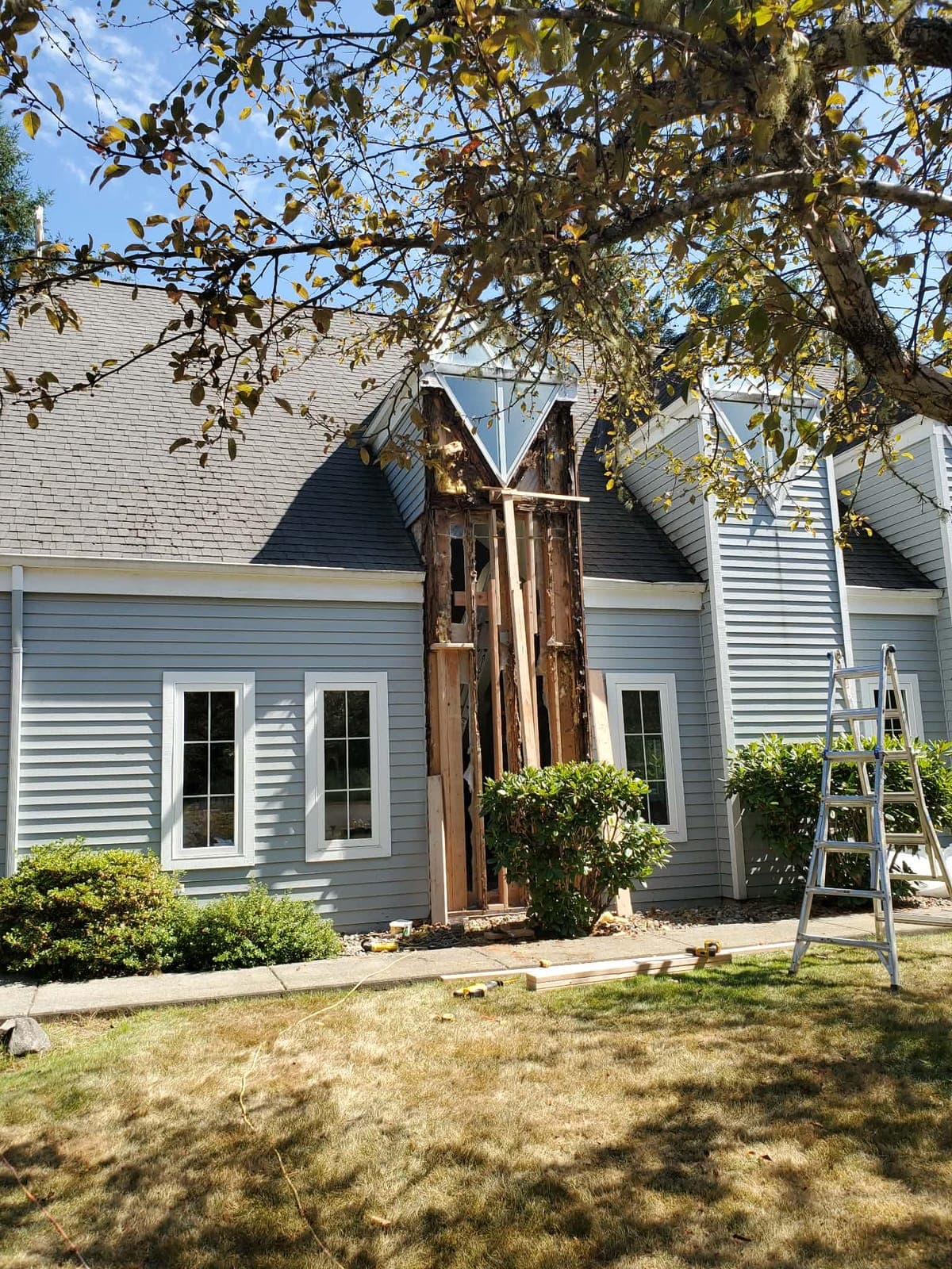 Section of lap siding removed from a home exterior, showing rebuilt wall framing, with a ladder alongside