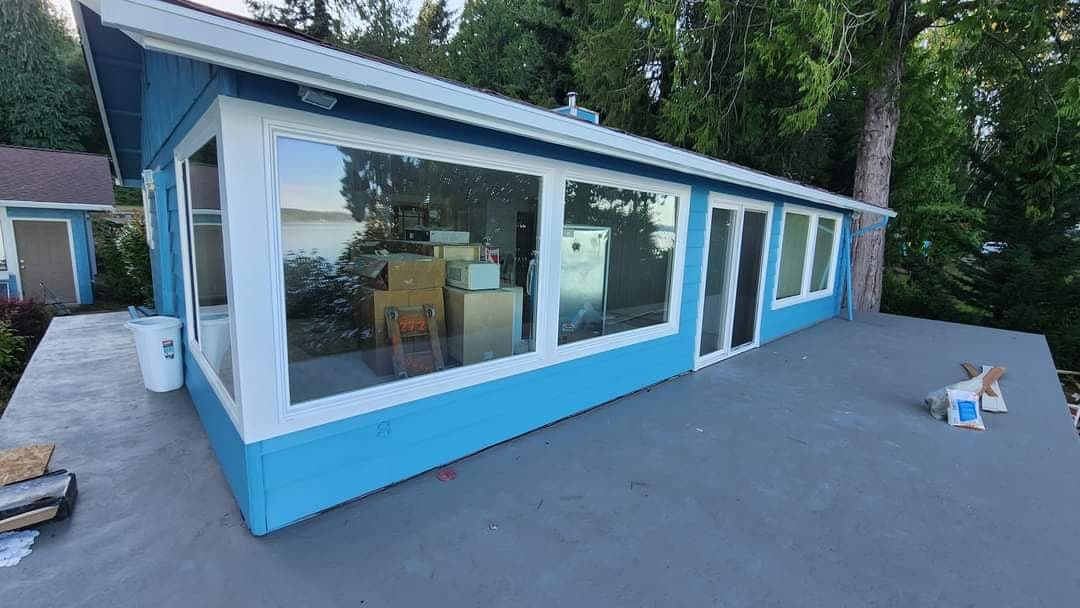 Blue-sided home with newly installed large picture windows and sliding glass doors facing a concrete patio